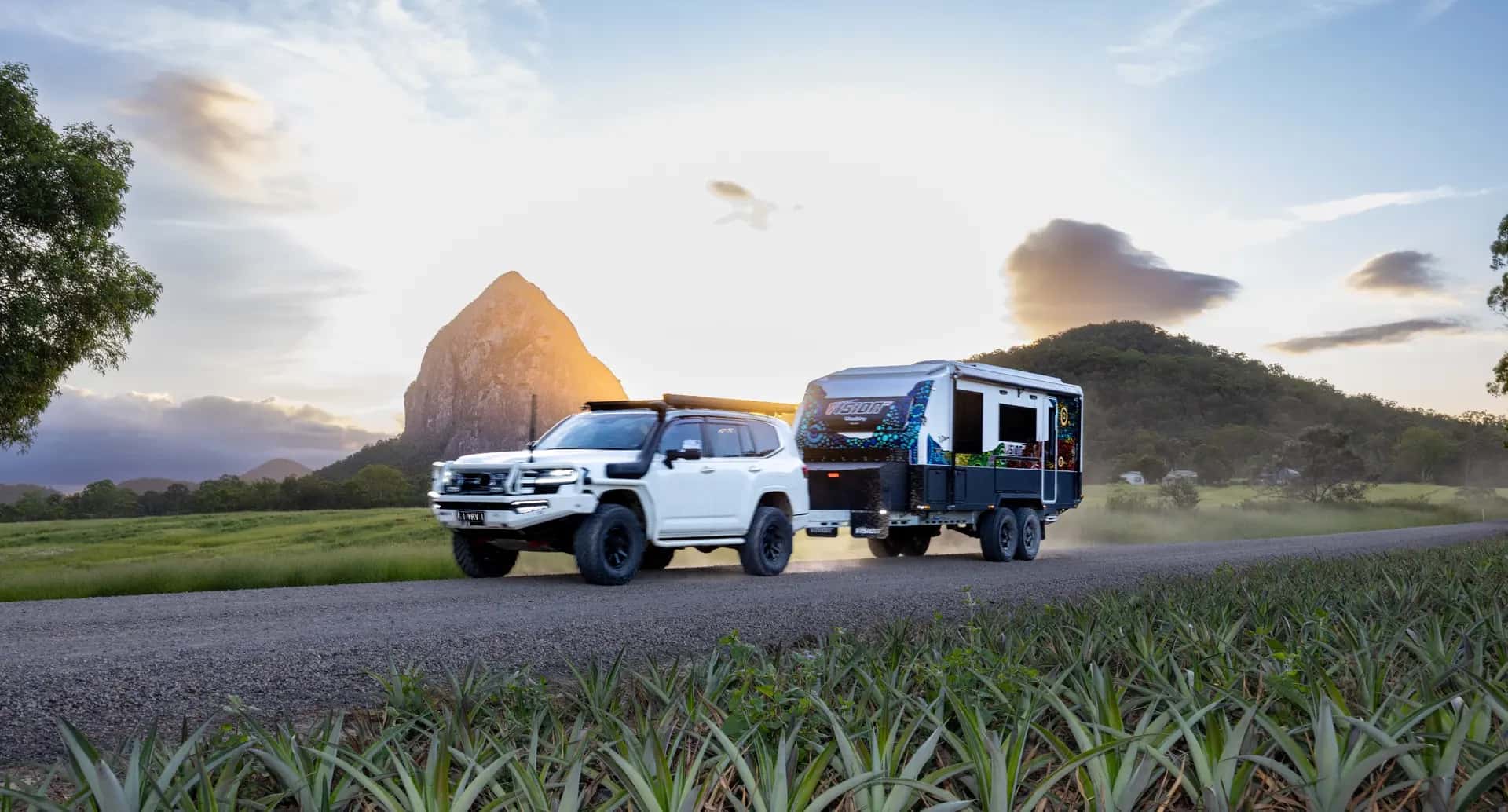 A Vision RV caravan towed on a gravel road below the Glasshouse Mountains